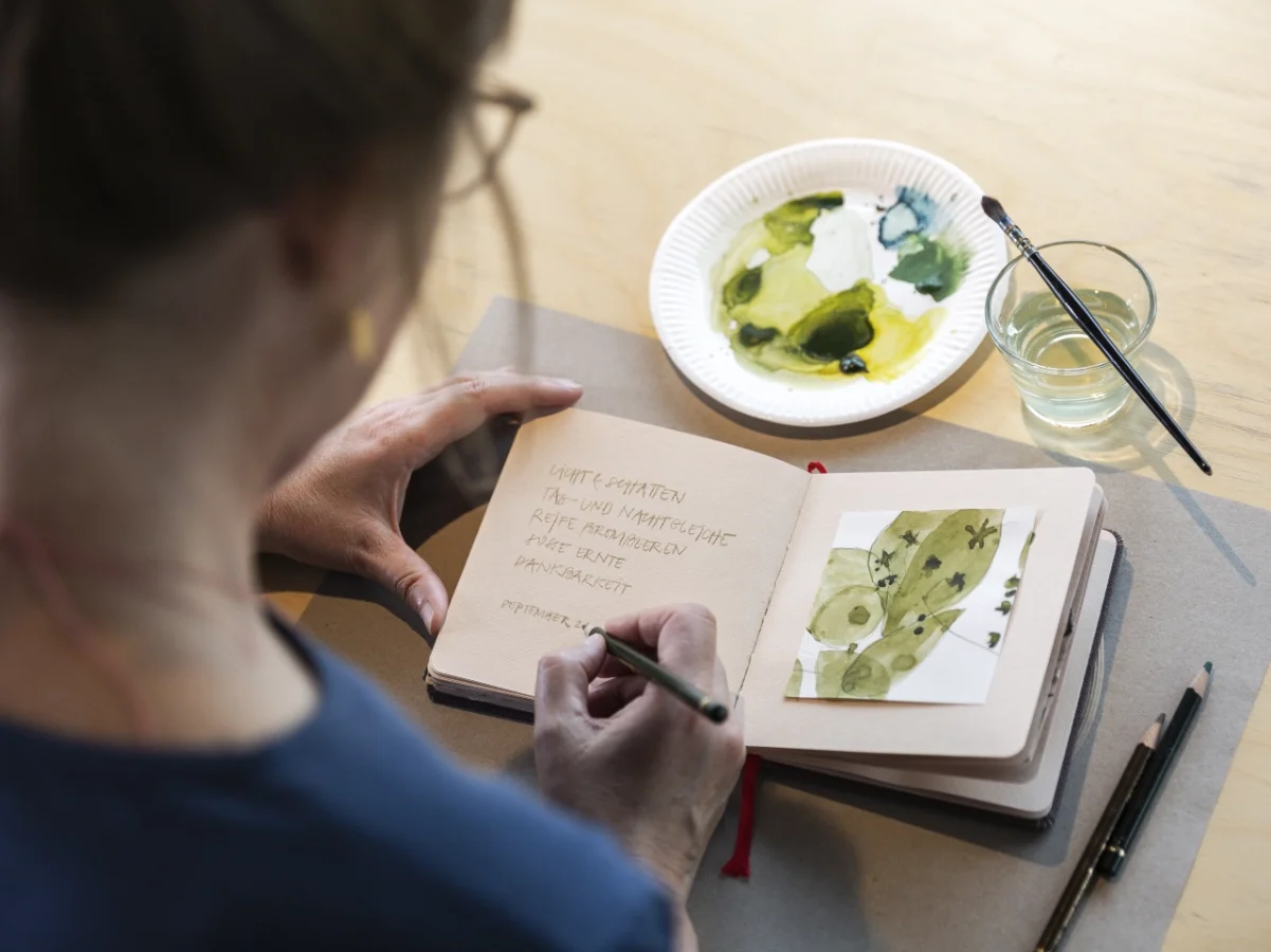 Frau malt in ihrem Bildertagebuch mit Aquarellfarbe.