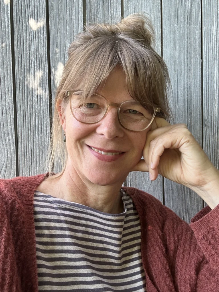 Sandra Baumann blickt vor einer Holzwand lächelnd in die Kamera.